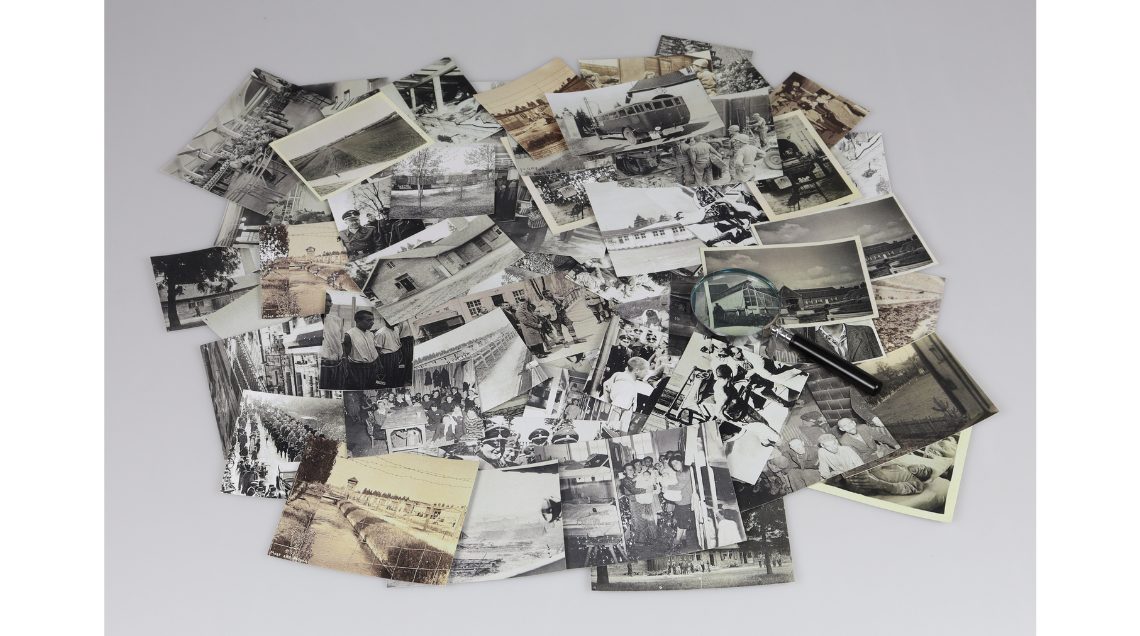 Foto: KZ-Gedenkstätte Dachau Fotografien in Schwarz-Weiß und Sepia, verteilt auf einer Fläche, zeigen historische Szenen und Personen aus verschiedenen Lebensbereichen. Eine Lupe liegt auf einigen Fotos.