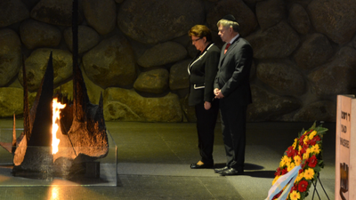 Karl Freller und Landtagspräsidentin Barbara Stamm in Yad Vashem 2014 Foto: Anton Preis Zwei Personen stehen vor einer ewigen Flamme in der Gedenkstätte Yad Vashem (Israel) mit Steinmauer im Hintergrund. Szene vermittelt feierlichen Moment des Gedenkens und Respekts.