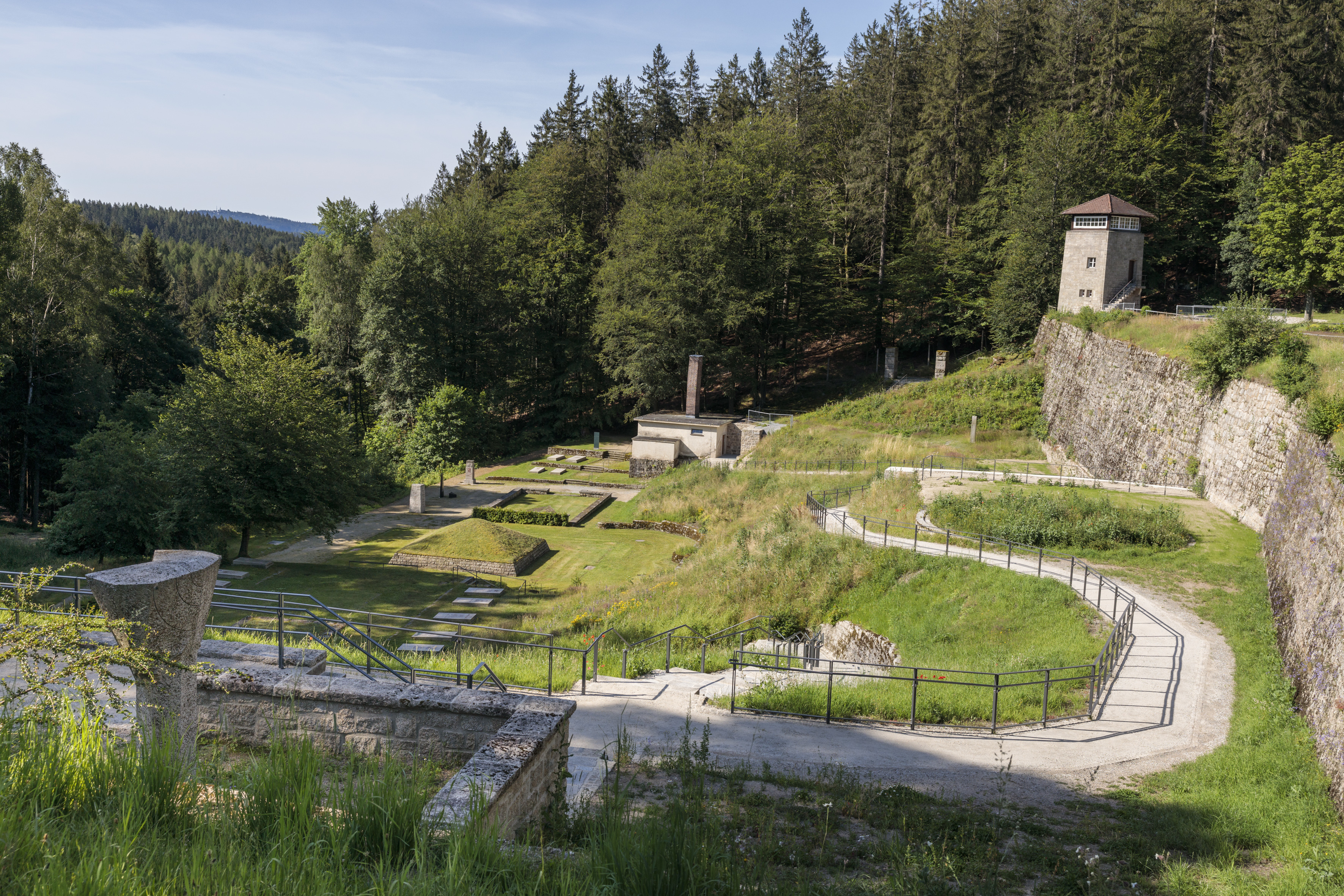 Tal des Todes Foto KZ-Gedenkstätte Flossenbürg / Th. Dashuber Fotografie einer historischen Grabanlage und Gedenkstätte mit sichtbaren Steinmauern, Wegen und einem Turm im Hintergrund, umgeben von Wald. Die Aufnahme zeigt das Tal des Todes, in dem heute der Opfer des KZ Flossenbürg gedacht wird.