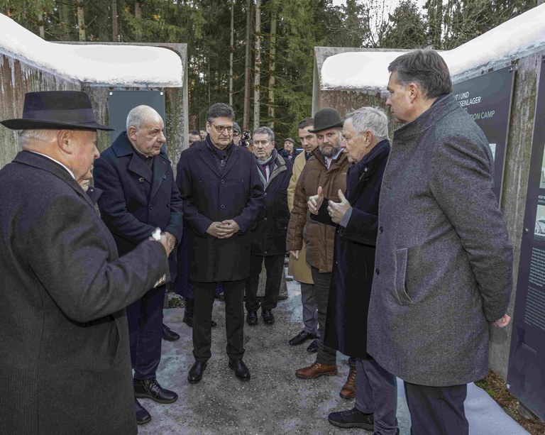Sechs Herren stehen am Gedenkort Massengrab im Mühldorfer Hart im Kreis und tauschen sich aus