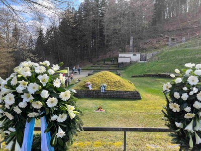 zwei Kränze mit weißen Blumen im Vordergrund. Dahinter Blick in das sogenannte "Tal des Todes" der KZ-Gedenkstätte Flossenbürg 