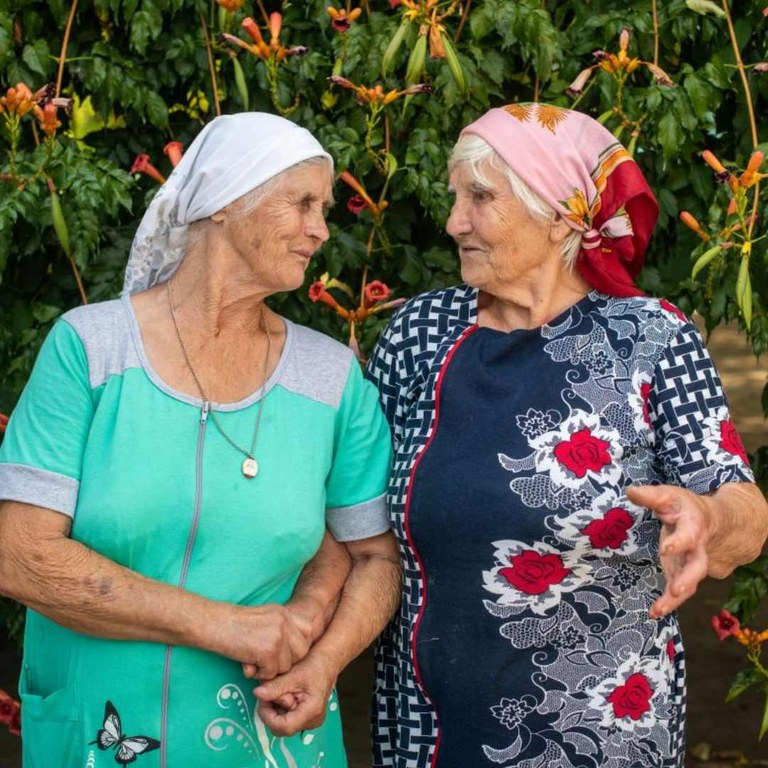 Das Bild zeigt zwei alte Frauen, die Schwestern sind, die sich anschauen. 