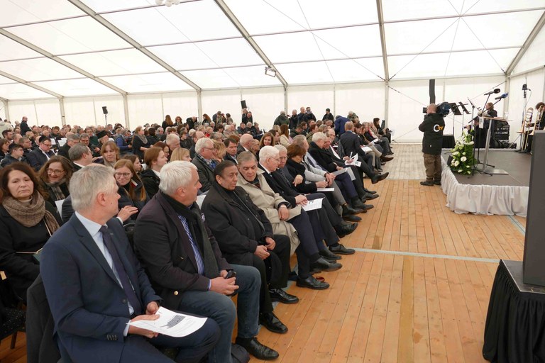 viele Menschen in Stuhlreihen, links ist eine Bühne im Bild. Die Gäste warten auf den Beginn der Veranstaltung